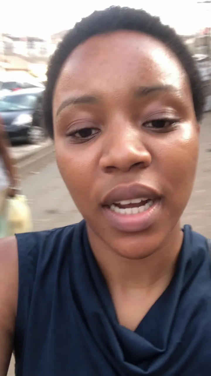 A woman talking to a phone camera while walking down a busy street in hazy daylight.